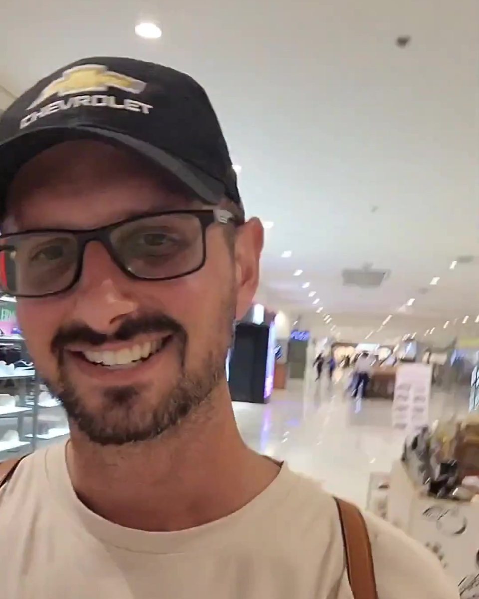 Todd Michael Gori in a dark cap, glasses and cream T-shirt in a mall